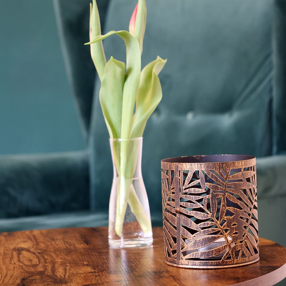 Teelicht-Dekoration neben einer Tulpe in einer Vase auf einem runden Holztisch mit einem petrolfarbenen Samt-Sessel im Hintergrund vor einer petrolfarbenen Wand